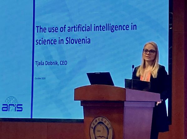 Direktorica ARIS predstavlja temo uporabe umetne inteligence v znanosti v Sloveniji na mednarodnem dogodku. Govori za govorniškim pultom, za njo pa je projekcijski zaslon s predstavitvijo.